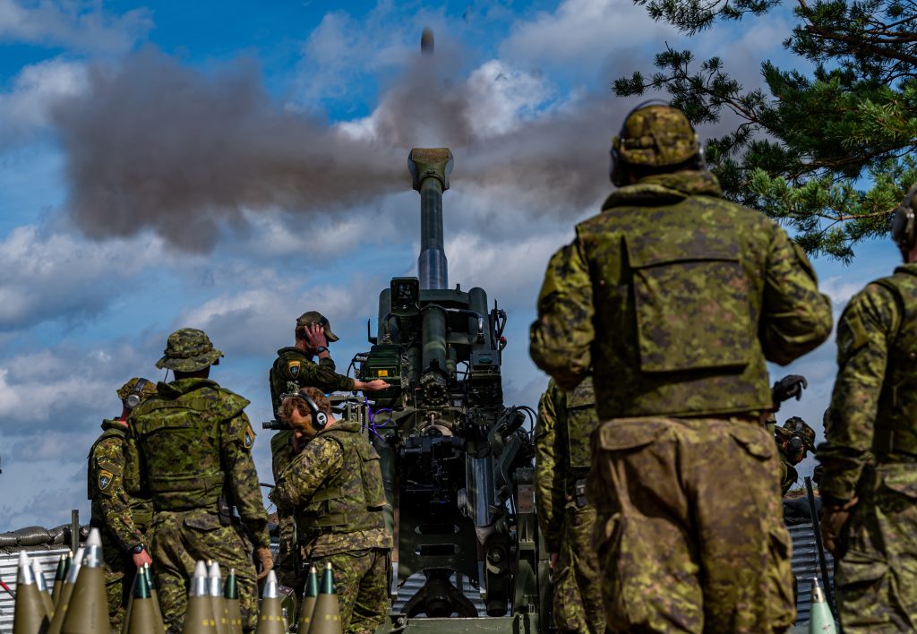 Canadian soldiers wearing camouflage fire a Howitzer gun in Latvia.
