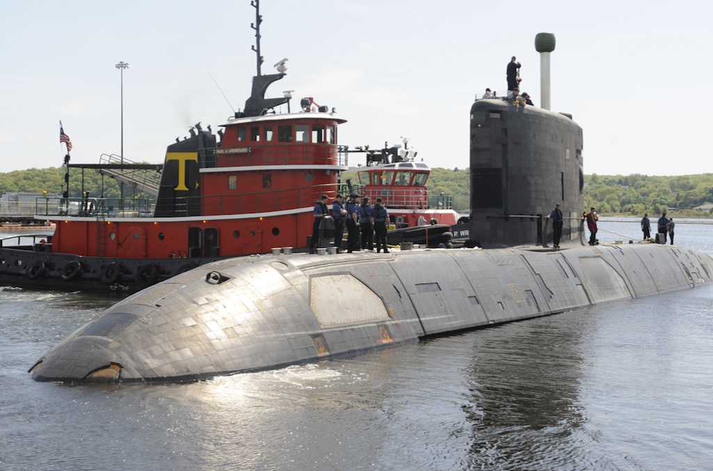 Several sailors stand on top of a submarine in port.