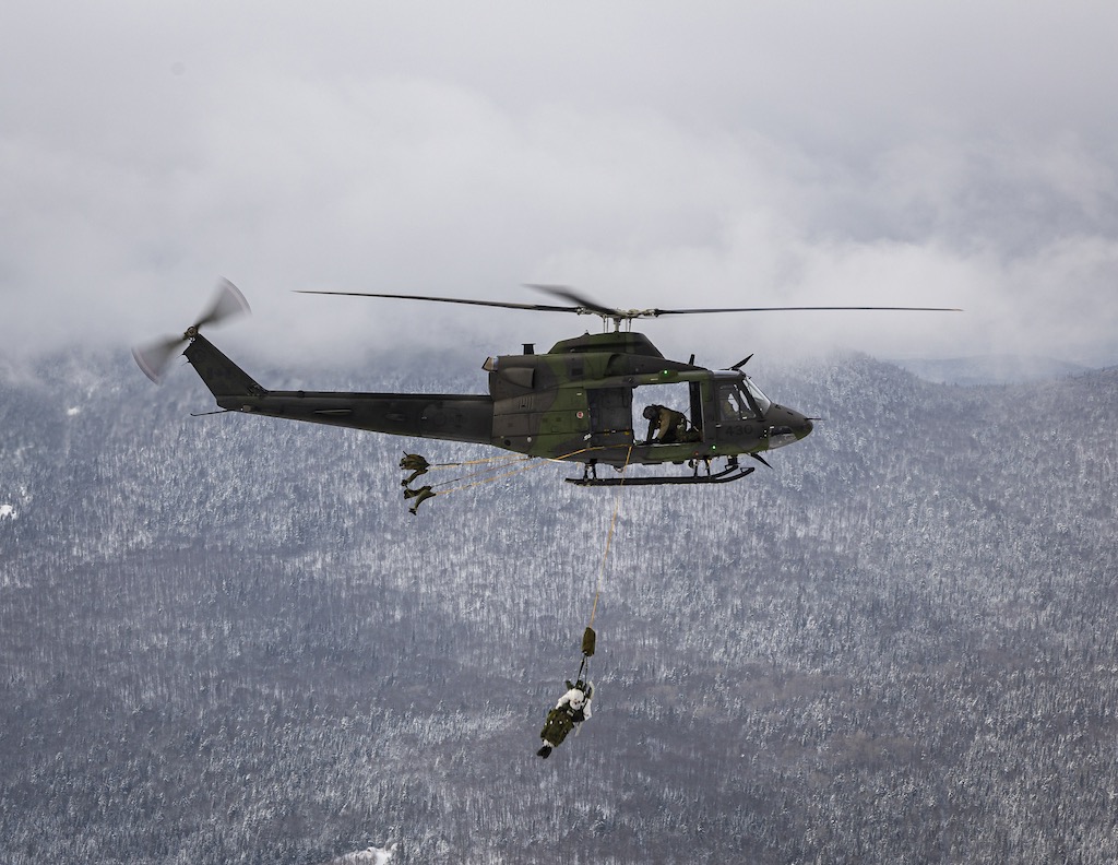 A Griffon helicopter soars over snowy treed mountains during a training exercise.