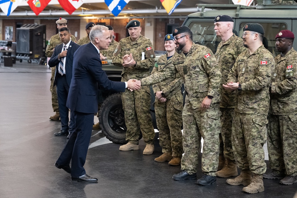 Prime Minister Carney shakes the hand of one of several Canadian troops, who are lined up to greet him.