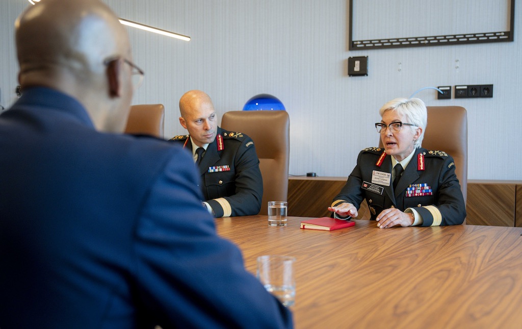 Three high-ranking military personnel are seated at a table in a meeting room.