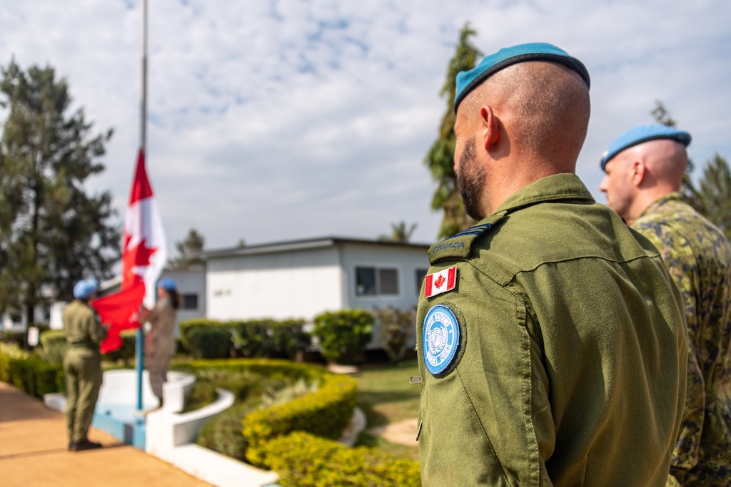 Armed forces member stand on parade as the Canadian flag is raised on a flag pole.