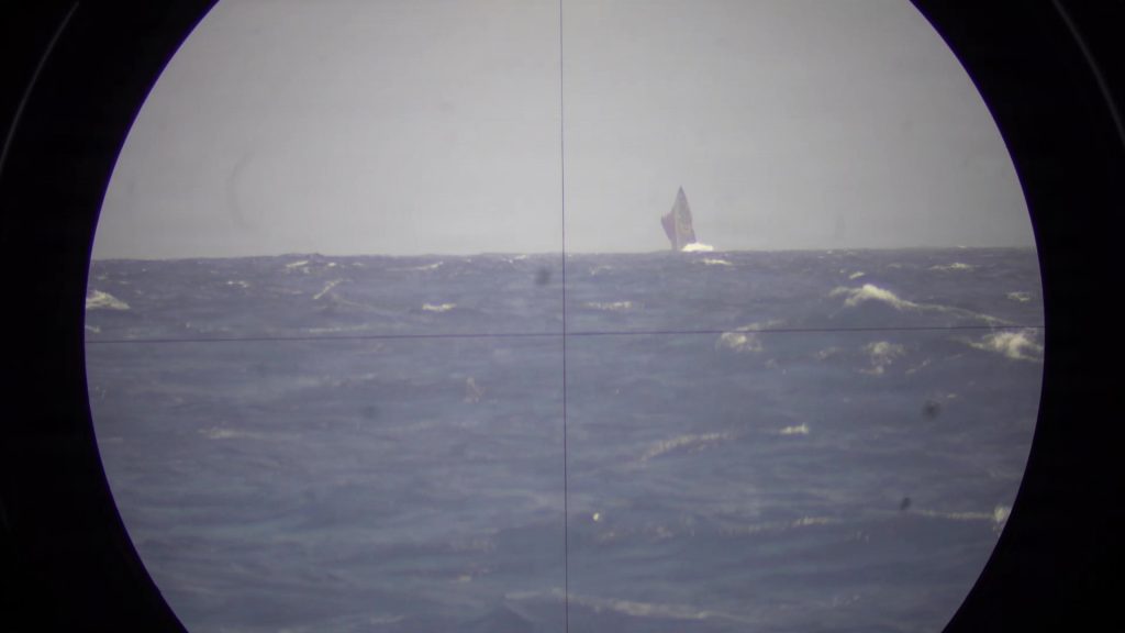 A circular view through a submarine's periscope of a submarine on the ocean's surface.