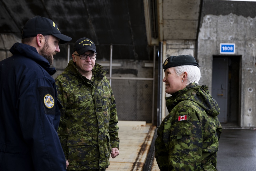 Two men and one woman in military clothing talk together.